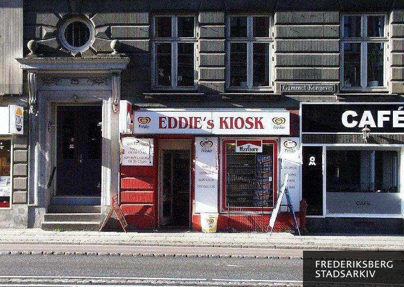 Butiksfacade til Eddie's Kiosk, der har udhængsskilt med cigaretreklame. Ved siden af ses indgangspartiet med mange gamle bygningsdetaljer og gadedøren til opgangen