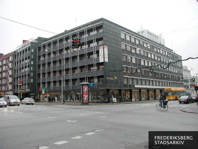 Hjørneejendommen Smallegade 2 og Falkoner Allé 1-5 med erhvervslokaler. Nordea har Frederiksberg Afdeling i Smallegade 2 . Der annonceres erhvervslokaler til leje på et reklamebanner på facaden på Falkoner Allé. Der er juleudmykning på Falkoner Allé, og bussen linje 18 ses. En mand cykler over krydset med et barn på cykelsædet bagpå. I baggrunden ses toppen af Falkoner Centret, hvor Radisson Blue Falkoner Hotel & Conference Centre ligger
