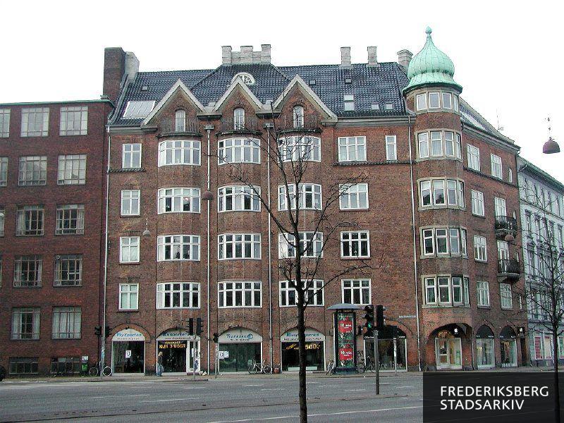 Hjørneejendommen med tårn på Julius Thomsens Gade 7 med butiksvinduer for FlyXperten og Eksperternes Trafikskole. På Åboulevard 15 hører butiksvinduerne til IT-udstyrbutikken Office Line i 2005. Foran ses en reklamesøjle