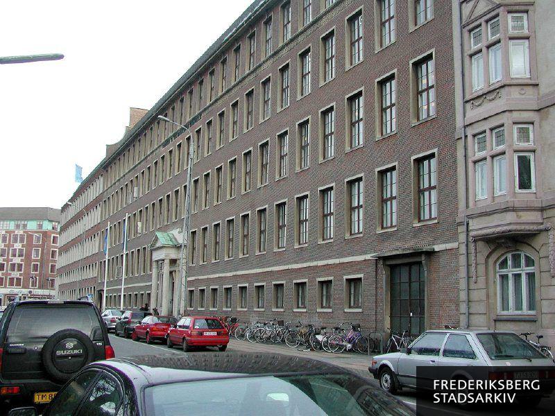 Niels Brocks Handelsgymnasium med HHX på Julius Thomsens Plads 6 i forgrunden og andre Niels Brock-afdelinger i nr. 8 og 10 med erhvervsuddannelser og efteruddannelser. Forrest ses parkerede biler og cykler i cykelstativer. I baggrunden ses Rosenørns Allé