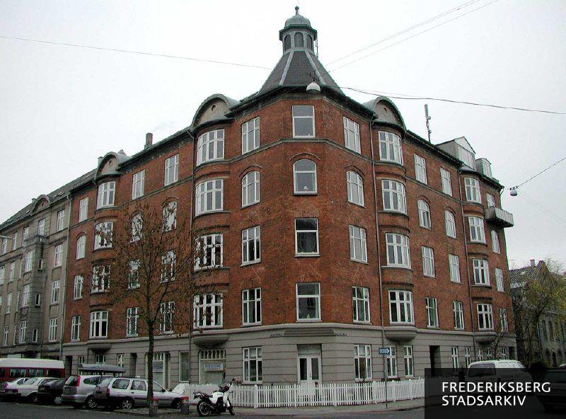 Hjørneejendommen Lykkesholms Allé 26 og Niels Ebbesens Vej 25 med tårn, karnapper og en altan i 2006, hvor servicevirksomheden Professionel Erhvervsrengøring har forretningslokaler i ejendommen. Etagetårnet har en lukket lanterne øverst. Der er nye vinduer i huset. En stor motorcykel og mange slags biler ses parkeret