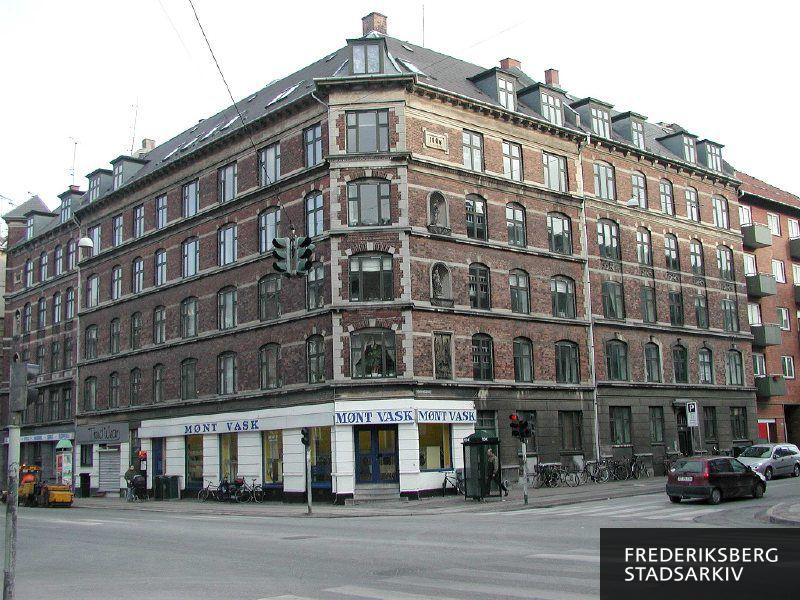 Hjørneejendommen Mariendalsvej 56 og Nordre Fasanvej 134 med skråt hjørne og mange detaljer, Bygningen har desuden rustikhjørne, figurer i nicher - og nederst et relief ligesom andre hjørneejendomme ved Nordre Fasanvej har. Mønt Vask i stueetagen har hvid facade, og der er en telefonboks på fortovet. Til venstre på Nordre Fasanvej står en gammel plakatsøjle med kobbertag