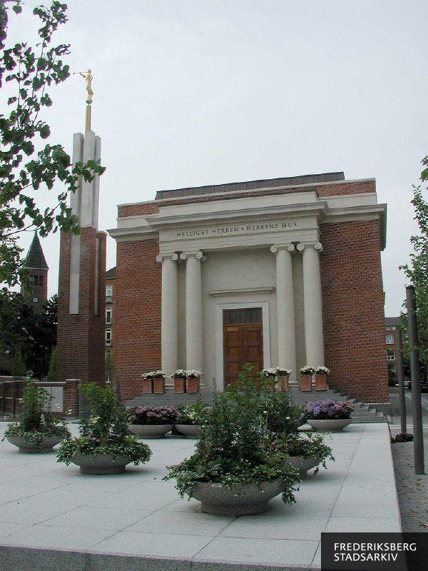 Jesu Kristi Kirke af Sidste Dages Hellige, The Church of Jesus Christ of Latter-day Saints, Copenhagen Denmark Temple. På fasciet står "Helliget Herren - Herrens Hus". Tårnet er 15 meter højt og fritstående, øverst står en forgyldt engel, der er  navngivet Moroni