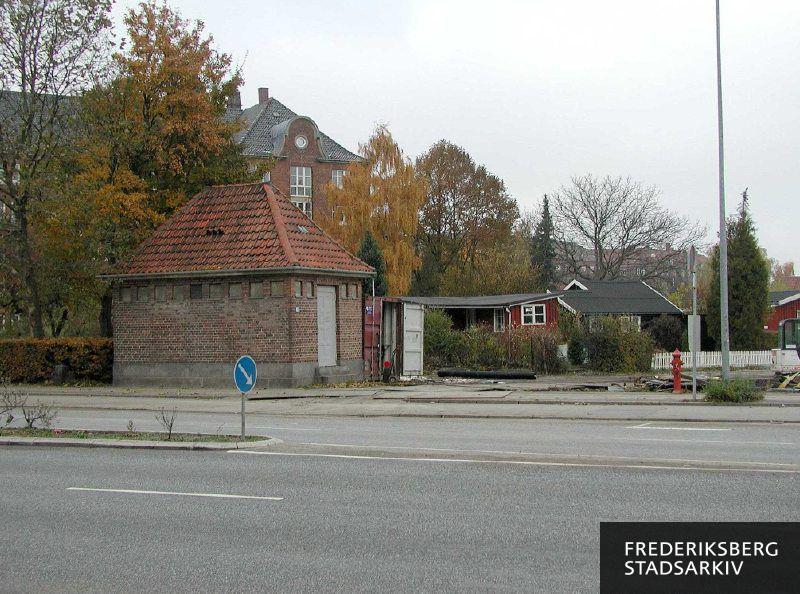 Et lille hus ved indkørslen til HF Dalgas kolonihaver, øverst til venstre ses gavlen på Dalgas Boulevard 1
