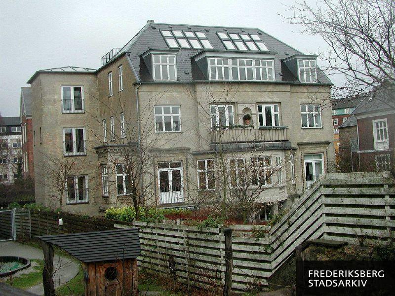 Ejendommens bagfacade med karnap, altan med niche, kviste og franske altaner til Sankt Jørgens Sø set fra stien Svineryggen, en tagterrasse mod vest skimtes øverst, længst til venstre ses lidt af hotellet Cabinn og nabohusets legeplads