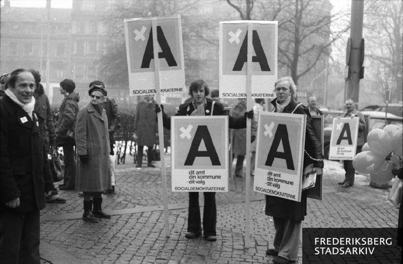 Tværpolitisk møde på Frederiksberg Rådhusplads i valgkampen op til kommunalvalget 7. marts 1978: Til venstre ses Anton Johannsen, formand for Slagteriforbundet, til højre ses socialdemokrater evt. DSU'ere med valgplakater på sandwichskilte og teksten Kryds ved A, dit amt, din kommune, dit valg.