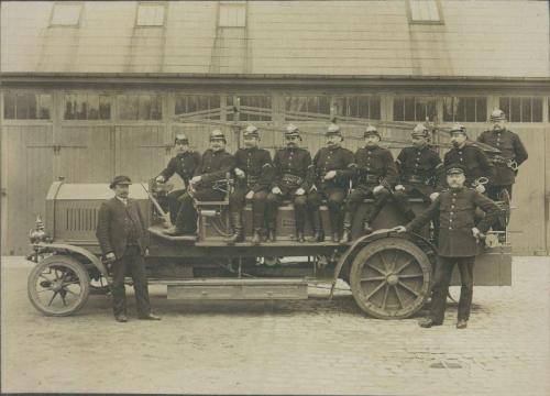 Brandfolk på  en tysk automobil motorsprøjte fra Fa. E. C., Jonstadt, i forbindelse med en demonstration af samme.
Fra venstre ses den tyske repræsentant, brandmændene nr. 41 Chr. Broholm, nr. 43 N. F. Vilh. Larsen, reservesprøjteførerne nr. 2 Alfred H. J. Brynildsen, nr. 24 Axel Helt og nr. 13 Ove Emil Petersen, brandmændene nr. 36 Chr. Fred. Caspersen, reservesprøjtefører nr. 18 Vilh. Rasmus Christoffersen, brandmændene nr. 42 Oscar Nielsen og nr. 17 Niels Lyngkjær. Stående er brandmand nr. 16 August Birgittus Troest.