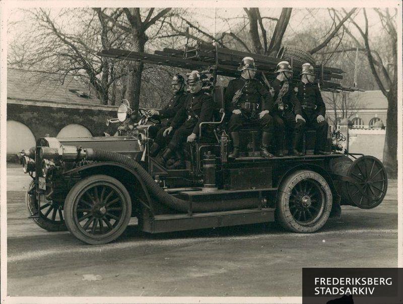 Brandfolk på en Dennis motorsprøjte P-1 på Frederiksberg Runddel. Fra venstre ses chauffør nr. 97 Lauritz Petersen, sprøjtefører V. Christoffersen, reservesprøjtefører nr. 35 Georg Petersen, brandmand nr. 124 H. Schwartzlose og brandmand nr. 85 Peter Elmer.