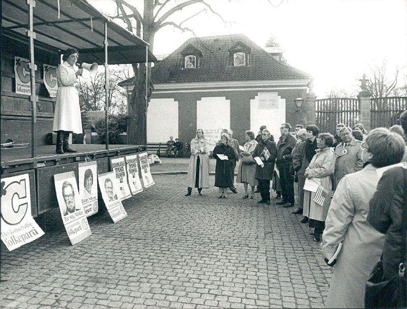 Det konservative kommunalbestyrelsesmedlem Lilian Nilsson holder valgtale på en blokvogn opstillet på Frederiksberg Runddel op til kommunalvalget 21. november 1989. Blandt tilhørerne er flest kvinder. Nogle vifter med flag, både dannebrog og det amerikanske flag