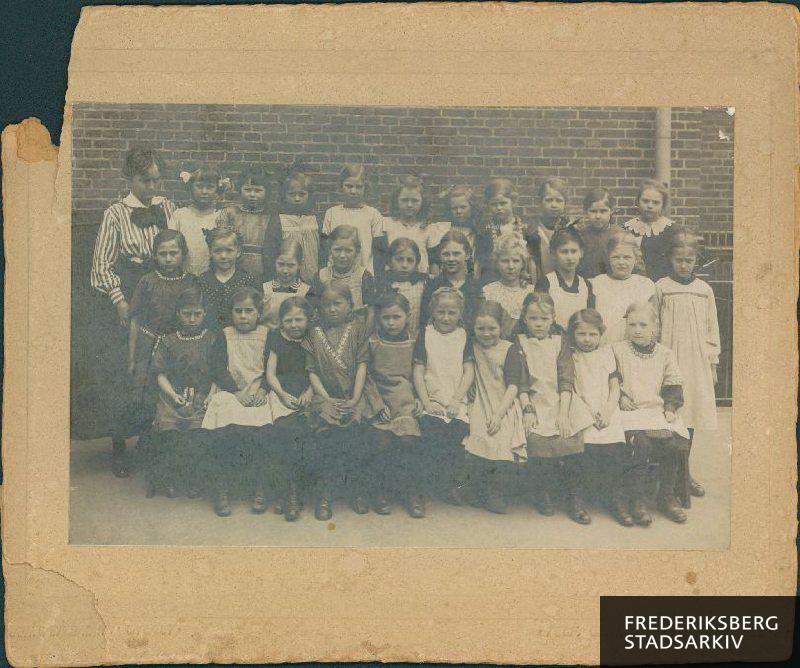 Pigeklasse, ca. 1910. Antageligvis Niels Ebbesens Skolen. 
Pigen på 1. række nr. 4 fra venstre er frk. Marie Olsen, sidst boende Keldgårdsvej 37 C, Valby. Lærerinden er antageligvis Frk. A. Bertram."