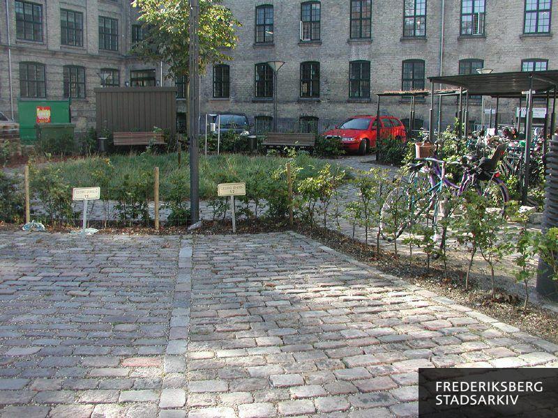 Private parkeringspladser og cykelstativer omkring et lille anlæg i gården ved Georg Jensen A/S til højre og Copenhagen Business School CBS til venstre
