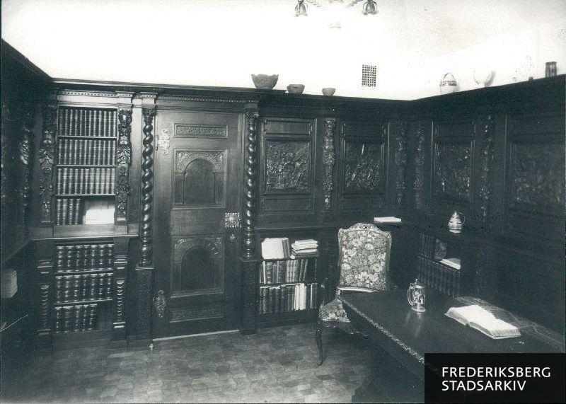 Interiør fra herreværelse i villa. Her er tudorpannelering (træfelter) i mandshøjde (før udførelsesforbud i 1920). Nogen steder er der brugt eg til døre og her er dørhåndtaget af smedejern. Andre steder er der til døre brugt mahogni og her er dørhåndtaget af messing. Ikke to er ens. Pejsen er af grøn og grå granit og rig på udskæringer. Der er bl.a. blde, der ikke kan ses, men som kun kan føles med hånden. I loftet er der stukkatur med kornaks