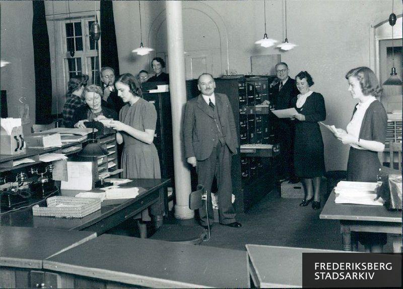 Frederiksberg Folkeregister, personalet i ekspeditionen, Falkoner Allé 7, ca. 1944.
Midt i billedet ses folkeregistrets leder, H.C. Hansen, og til højre ved kartoteksskabet ses Hugo Nielsen og Fru Andersen
