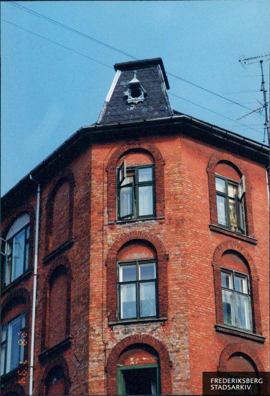 Hushjørnets øverste etager og det franske tårntag ses i juli måned mod en blå himmel. Ejendommen med de blændede vinduer og antenner på taget er fra 1897