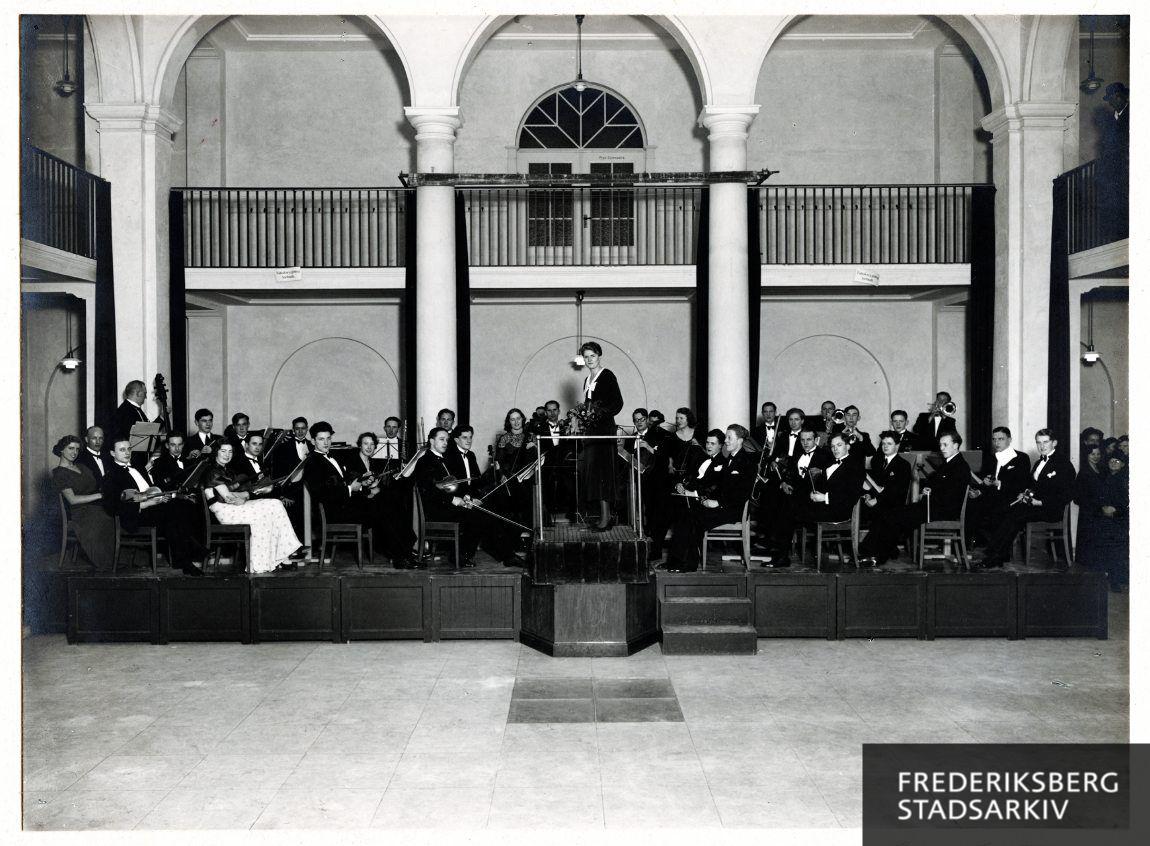 Grethe Kolbe dirigerer Frederiksberg Kommunale Fortsættelseskursus' orkester i Lindevangskolens aula