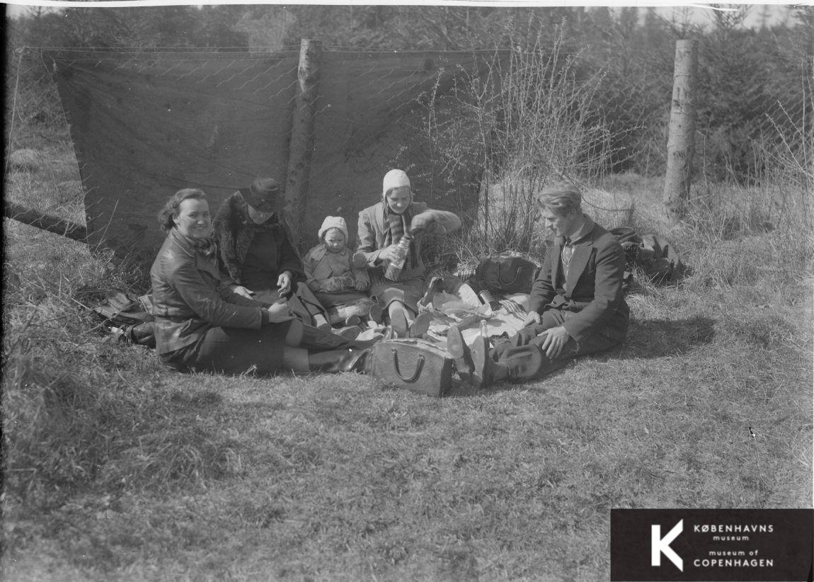 En familie har indrettet sig med tæpper og kaffe på en skovtur i det fri